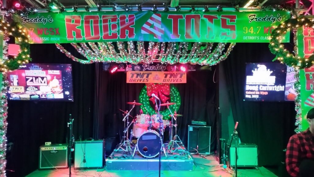 Live event stage setup for Rock 4 Tots with drums, guitars, microphones, and colorful lighting